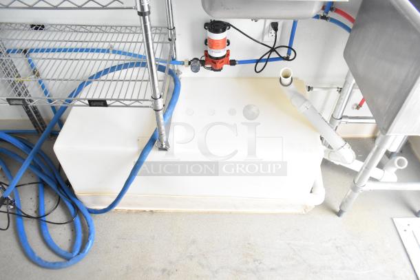 Interior view of Nationwide 24' shell food trailer, showcasing installed shelving, plumbing, white tank, and blue hoses.