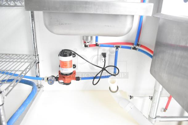 Interior of a Nationwide 24' Shell Food Trailer showing under-sink plumbing, wiring, and installed water pump system.