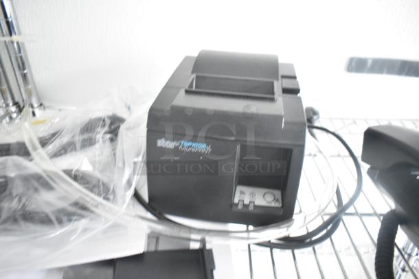 Star Micronics TSP100III thermal receipt printer in black, placed on a metal shelf, partially covered with clear plastic, power cord attached.