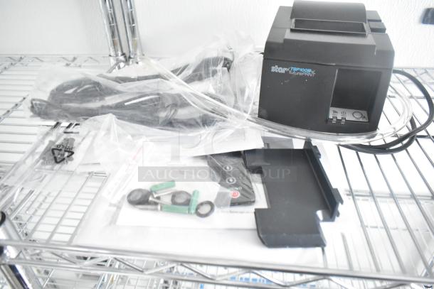 Star Micronics TSP100III receipt printer, black, on a metal shelf with cables and components in plastic bags.