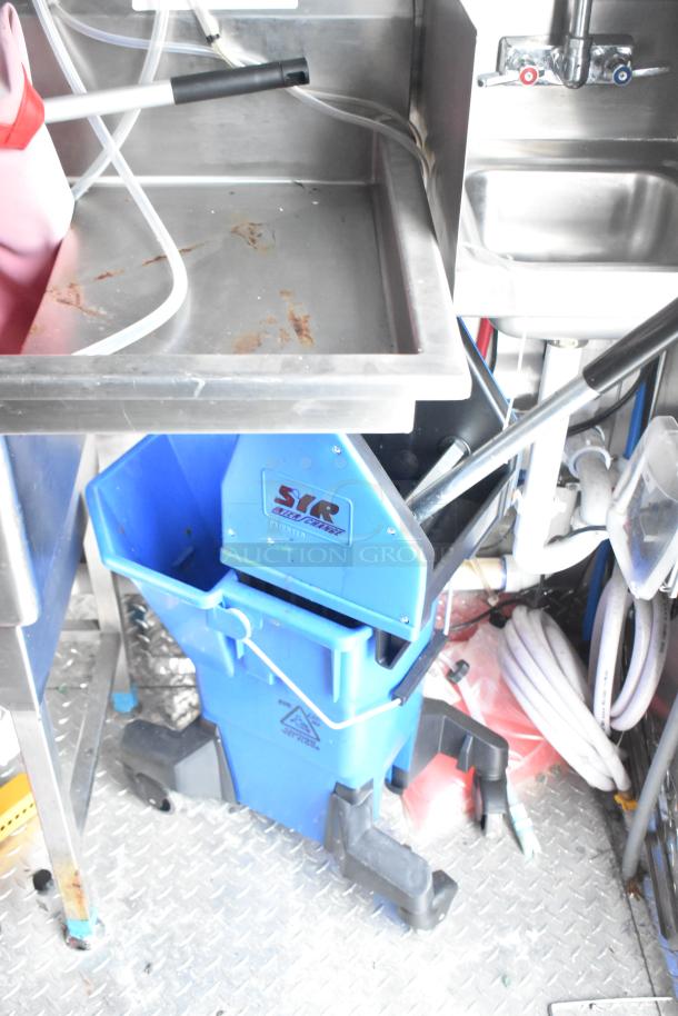 Interior of a 2021 Titanium Cargo 28' food trailer showing sinks, integrated plumbing, grease hood, and blue mop bucket.