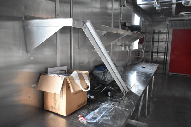 Interior of a brand new 2021 Titanium Cargo 28' food trailer, featuring metal shelving, workspace, and integrated systems.