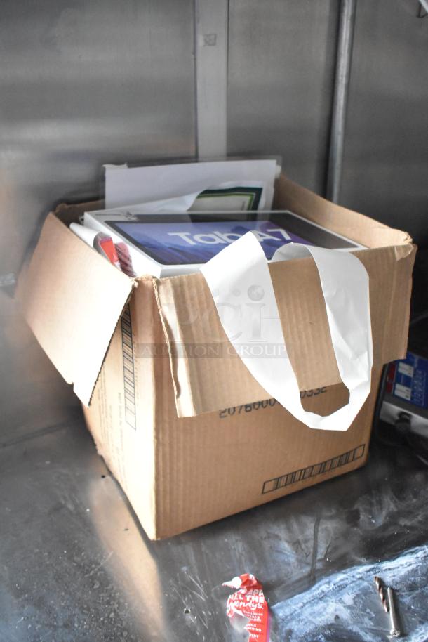 Cardboard box containing paper and a tablet packaging labeled "Tab A7" inside a metal trailer interior.