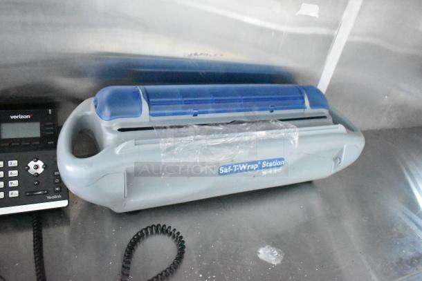 Gray Saf-T-Wrap Station with blue cover on stainless steel counter, next to black Yealink phone.