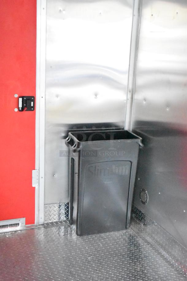 28' Titanium Cargo food trailer interior showing sleek aluminum walls, red door, and built-in black trash bin. Ideal for custom mobile kitchen.