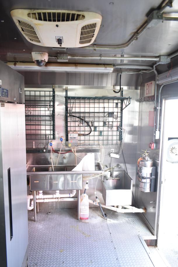 2020 Continental Cargo 8.5x28 mobile kitchen interior with sinks, plumbing, hood system, and fire extinguisher; equipped for commercial use.