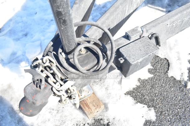Trailer hitch assembly on snow-covered ground, featuring chains and cables. Part of Rock Solid Cargo fast-food trailer.