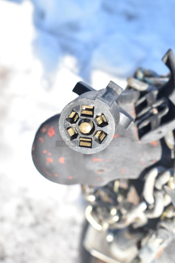 Close-up of a black metal trailer hitch connector, showing the electrical plug with several pins, part of the Rock Solid Cargo trailer.