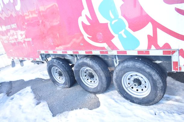 Red food trailer with graphics and text for fast-food delivery, showing three wheels and visible wear. Ideal for mobile kitchen use.