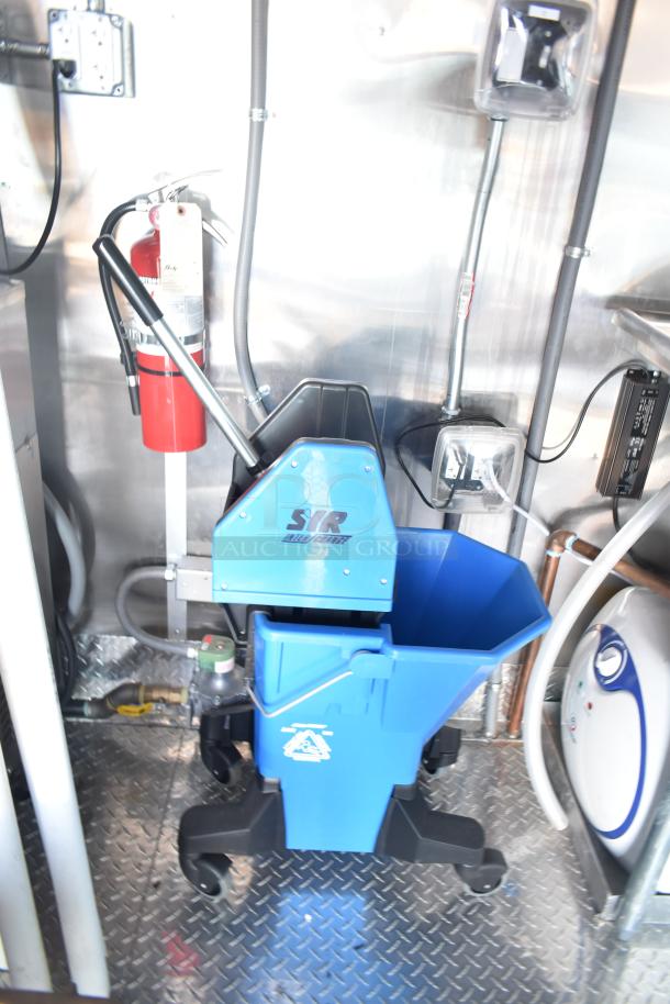 Blue SYR AutoCharge cleaning system and fire extinguisher inside Rock Solid Cargo fast-food trailer, featuring diamond plate flooring.
