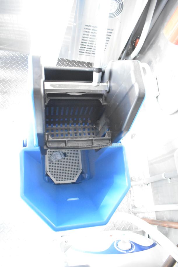 Mobile kitchen trailer interior with blue cleaning station, featuring mop bucket and wringer, on diamond plate flooring.