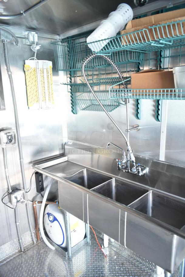 Stainless steel sink with commercial faucet in Rock Solid Cargo fast-food trailer. Features shelving and plumbing.