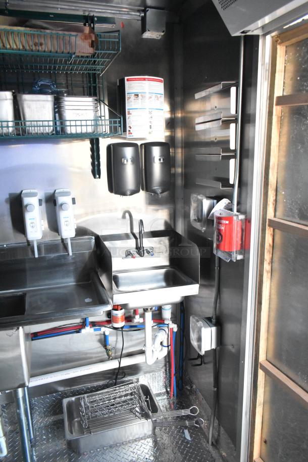 Interior view of a Rock Solid Cargo fast food trailer with stainless steel sink, soap dispensers, and shelving for kitchen utilities.