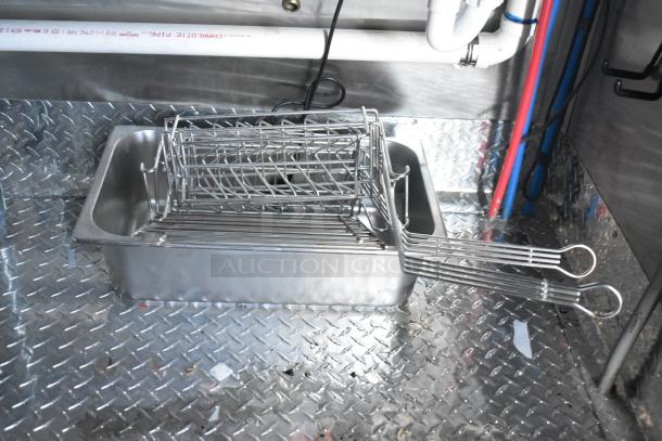 Commercial-grade metal fry basket and tray on diamond plate flooring in a fast-food trailer kitchen.