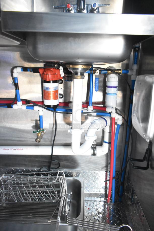 Rock Solid Cargo fast food trailer sink area; visible plumbing with SEAFO water pump, pipes, and metal diamond plate flooring.