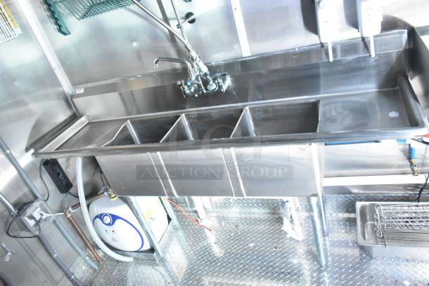 Stainless steel multi-compartment sink in Rock Solid Cargo mobile kitchen trailer, featuring commercial fixtures and plumbing.
