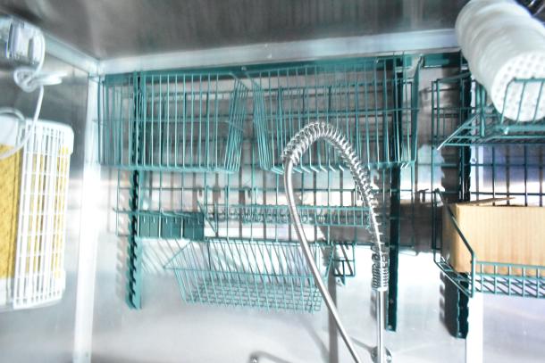 Interior of Rock Solid Cargo fast-food trailer showing teal metal shelves and a flexible sprayer faucet.