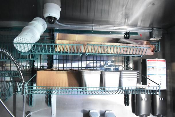 Interior view of a Rock Solid Cargo fast food trailer. Features wire shelving, bins, and a surveillance camera. Ideal for high-volume service.