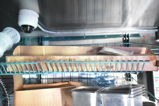 Interior view of Rock Solid Cargo fast-food trailer with wire shelves, trays, a dome camera, and stainless steel containers.