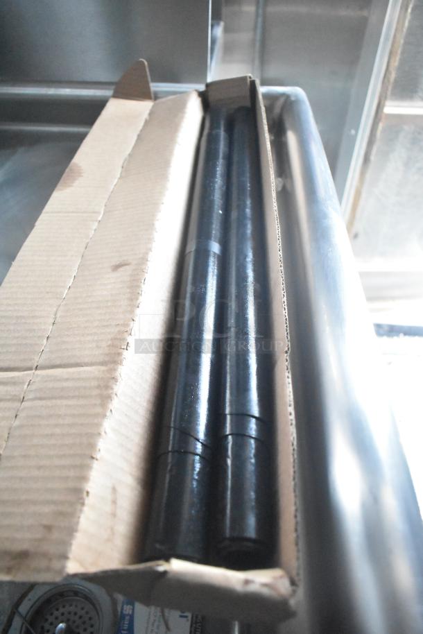 A cardboard box containing black cylindrical pipes, part of equipment in a Rock Solid Cargo mobile kitchen.