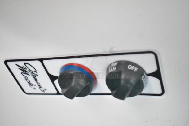 Close-up of Coleman-Mach control panel with temperature and fan speed knobs, showing settings for air conditioning in a mobile kitchen.