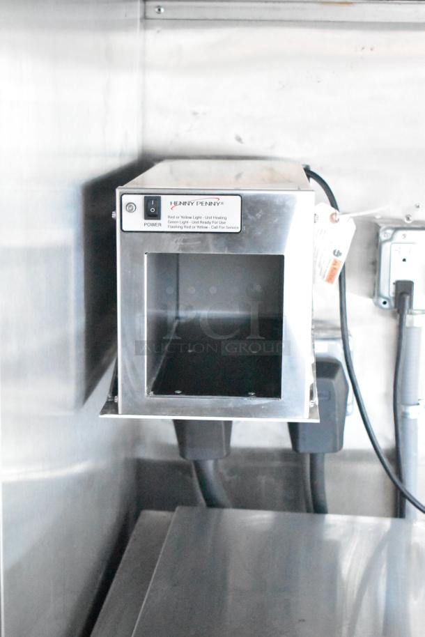 Henny Penny gas fryer control panel in a stainless steel mobile kitchen. Power switch and status lights visible.
