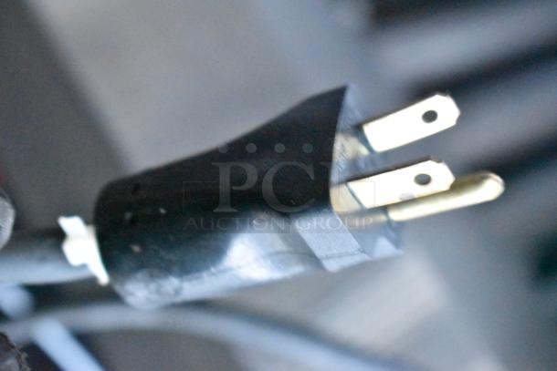 Close-up of a standard three-prong electrical plug, showcasing prongs and cable, against a blurred background.