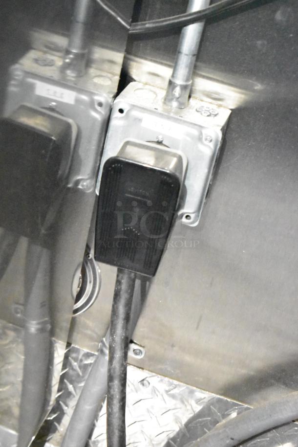 Electrical outlet with industrial-grade plug and cable inside the Rock Solid Cargo fast food trailer. Reflective surfaces visible.