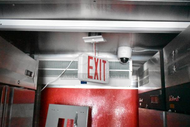 Interior of Wendy's-style fast-food trailer showing EXIT sign, commercial equipment, and security camera in a stainless steel setting.