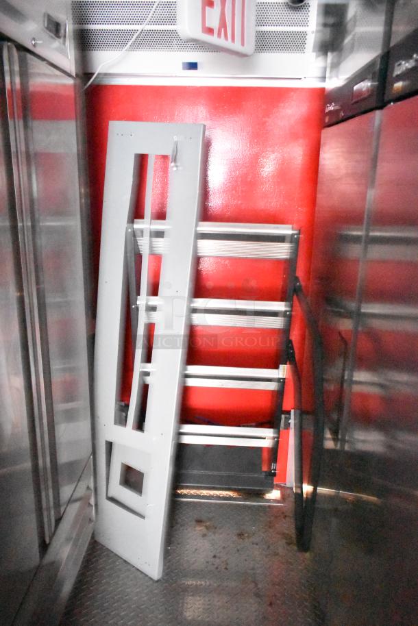 Interior of a Rock Solid Cargo fast food trailer showing industrial metal shelving against a red wall and an EXIT sign.