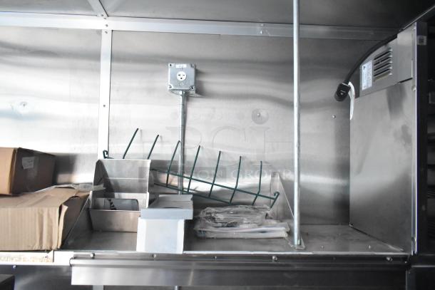 Interior of Rock Solid Cargo mobile kitchen trailer, showing stainless steel surfaces, storage shelves, and electrical outlet.