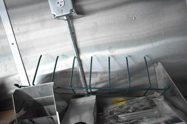 Interior detail of Rock Solid Cargo fast food trailer. Features include electric socket, metal shelf, and container. Ideal for mobile kitchen setup.