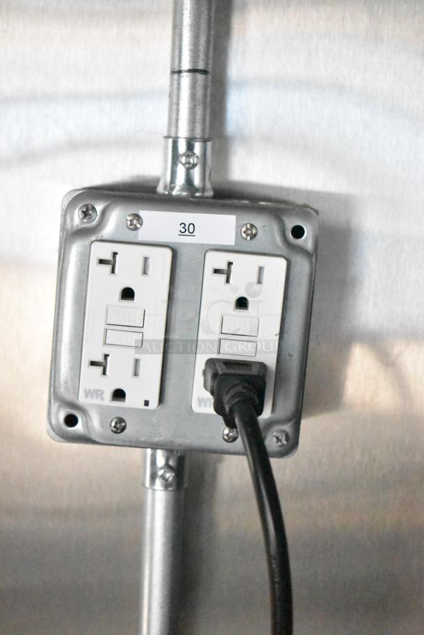 Electrical outlet in Rock Solid Cargo mobile kitchen trailer, labeled "30," with a black cord plugged in.