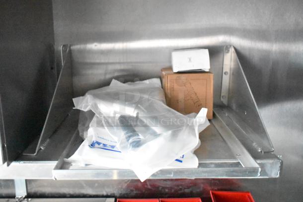 Stainless steel shelf inside Rock Solid Cargo fast food trailer with packaged equipment and a brown box marked "DICIN".