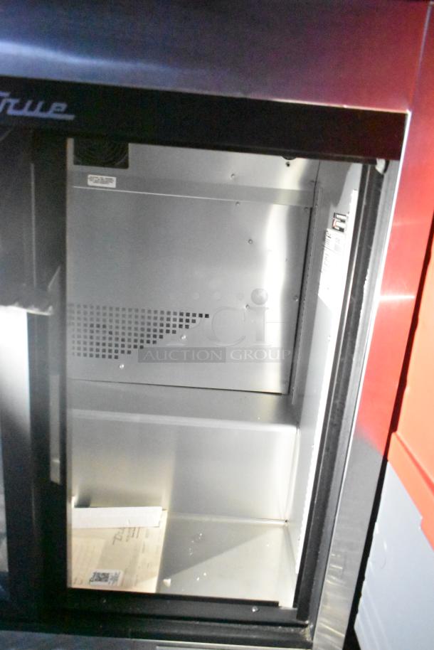 Interior of a mobile kitchen fridge with the "True" brand label. The stainless steel interior is clean and empty.