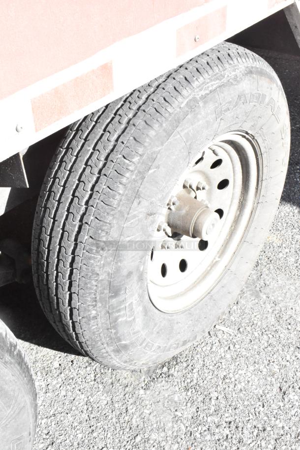 Trailer tire on gravel, attached to a 28' Wendy’s mobile kitchen. Tire shows wear but appears functional.