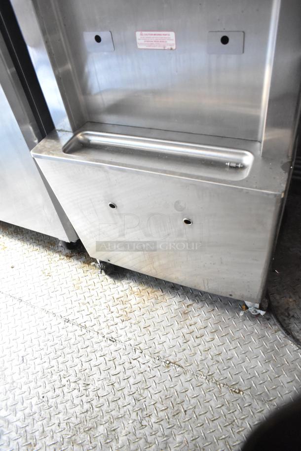 Stainless steel commercial fixture in a 28' fast food trailer, featuring smooth metal surface, sturdy construction, wheels, and a caution label.