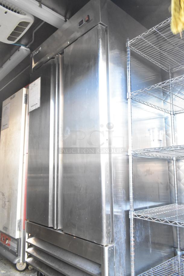 Stainless steel commercial freezer in a mobile kitchen trailer, featuring a double-door design with cooling vents.