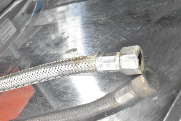 Close-up of braided metal hose on La Cimbali M29 espresso machine. Stainless steel texture, slight tarnish on connector.