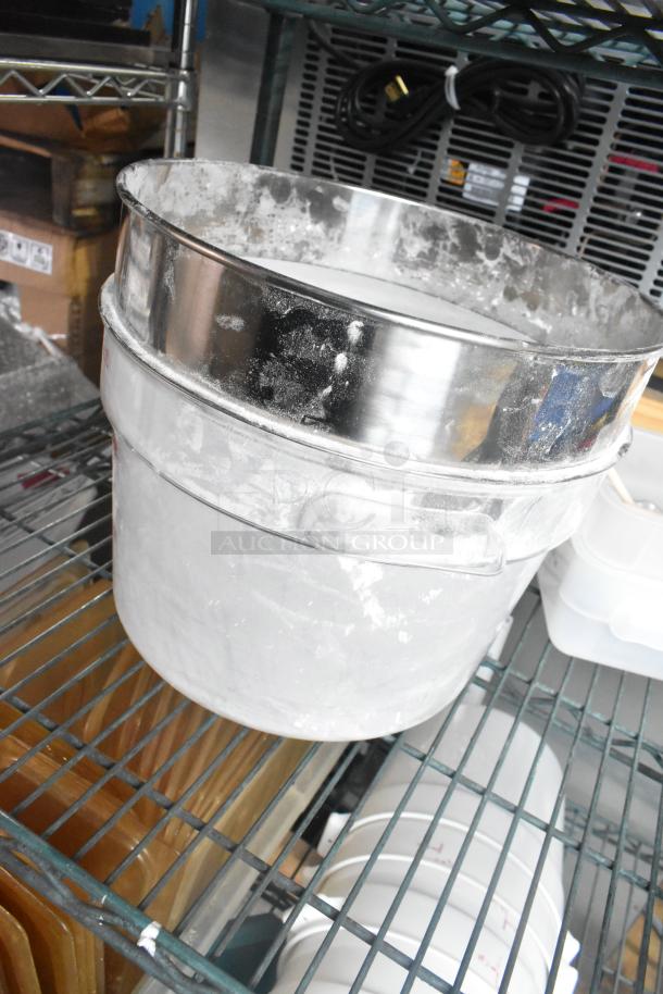 Three-tier shelf with various items including metallic coffee pots and poly cylindrical bins. Some surfaces show signs of wear.