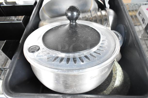 Various kitchen items in a bus bin, featuring a Svebake metal bowl with vented lid, on a black poly rack.