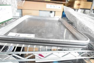 Three metal half-size baking pans stacked on a shelf. Slight wear visible, with auction tag labeled "72 QTY."