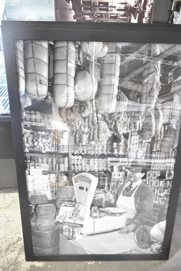 Framed black and white photo of a vintage deli counter with hanging meats, jars, and a scale. Vintage market scene.