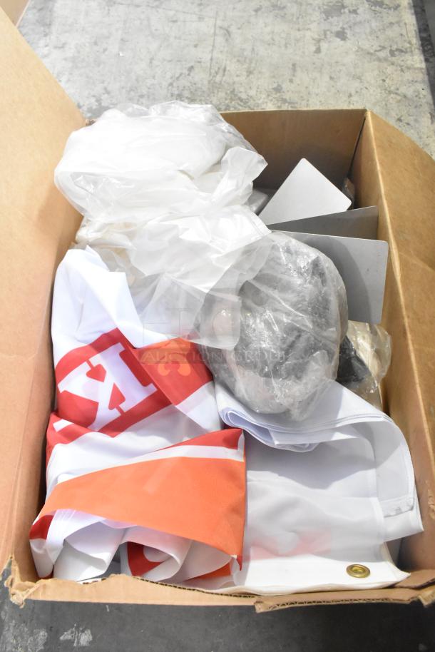 Cardboard box with mini clipboards, plastic-wrapped items, and a red and orange flag, suggesting a mixed item lot.