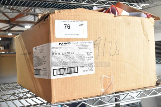 Cardboard box labeled "Popeyes 4.25” Brioche Bun, Sliced" with quantity 96. Auction tag "76 QTY" from PCAuctions.com attached. Box condition is slightly worn.