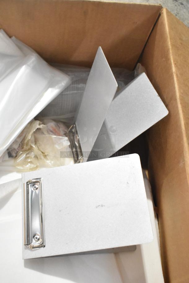 Lot of items in a box includes several silver mini clipboards and various materials. Condition appears used.