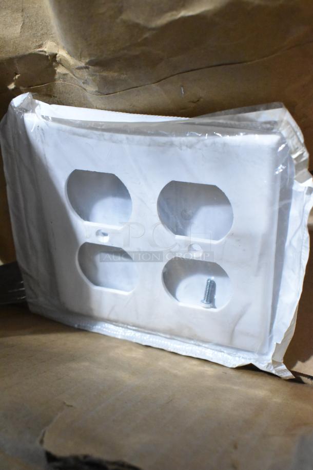 Lot of various items, including an unused white outlet cover in packaging, with metal screw, on brown cardboard.