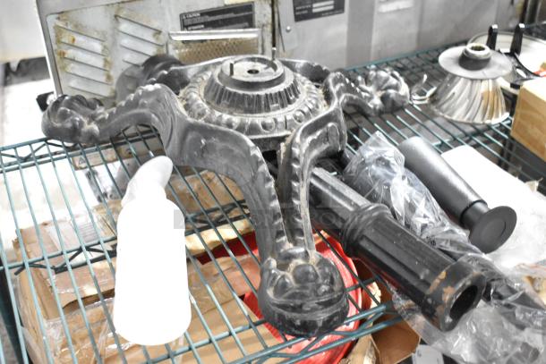 Lot of various items on wire shelf, including ornate black metal stand, white bottle, and unidentified parts. Mixed condition.