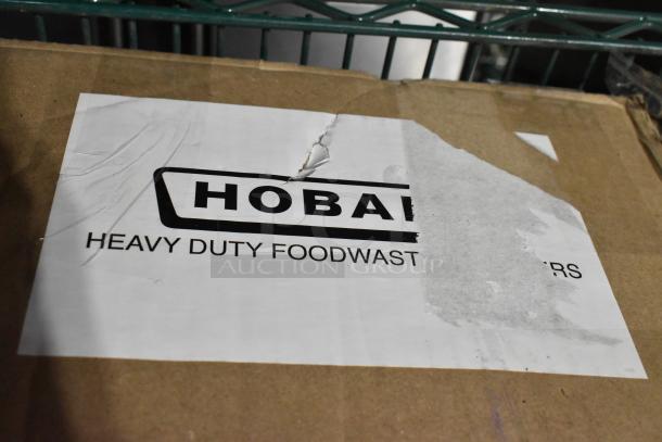 Cardboard box with "Hobart Heavy Duty Foodwaste Disposers" label, indicating a scratched and dented commercial garbage disposer inside.