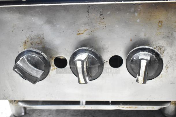 Commercial countertop gas-powered charbroiler grill, stainless steel, three control knobs, visible wear, for professional kitchens.